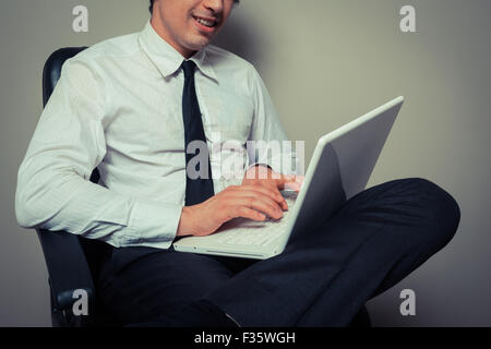 A young businessman is sitting in an office chair and is working on laptop computer Stock Photo