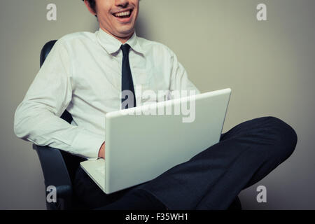 A young businessman is sitting in an office chair and is working on laptop computer Stock Photo