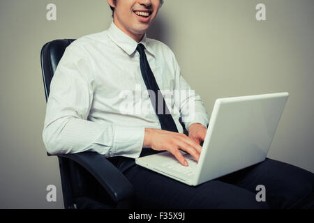 A young businessman is sitting in an office chair and is working on laptop computer Stock Photo