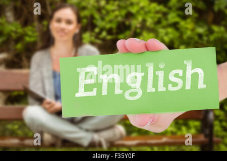 English against smiling student sitting on bench listening music with mobile phone and holding book Stock Photo