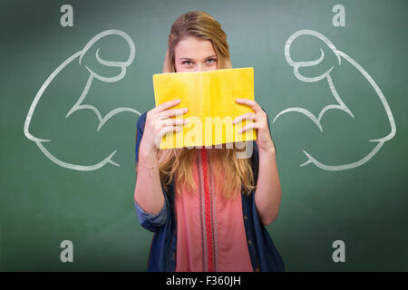 Composite image of student covering face with book in library Stock Photo