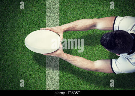Composite image of high angle view of man holding rugby ball with both hands Stock Photo
