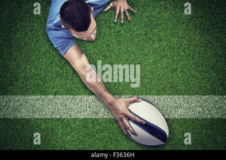 Composite image of rear view of rugby player lying in front with ball Stock Photo