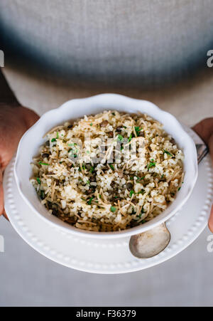 A bowl of bulgur pilaf mixed in with lentils and fresh herbs are in the hands of a man wearing an apron. Stock Photo