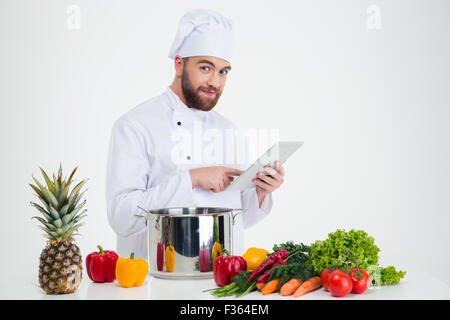 Portrait of a happy male chef cook using tablet computer while preparing food isolated on a white background Stock Photo