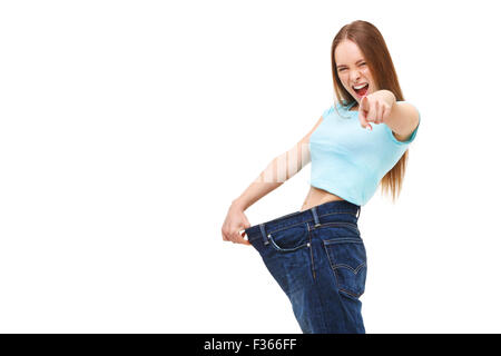 You can do it! Young slim woman with large jeans pointing finger at you - isolated on white background. Stock Photo