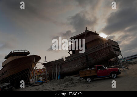 The unfinished wooden fishing vessels are seen during the sunset in an artisanal shipyard on the beach in Manta, Ecuador. Stock Photo