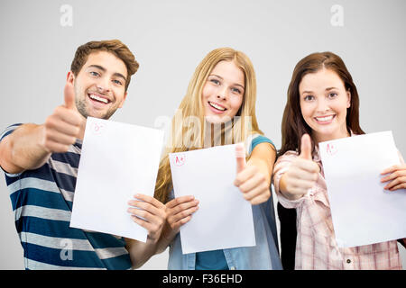 Composite image of students holding up exam and doing thumbs up Stock Photo