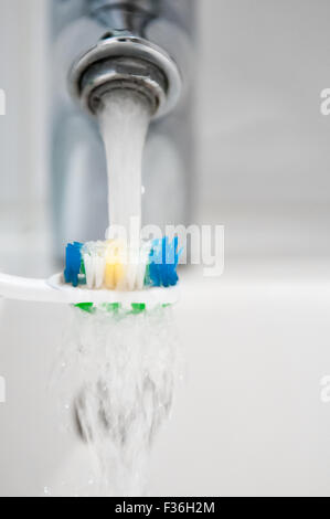 Toothbrush being rinsed under running water from a tap Stock Photo