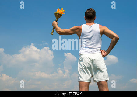 Athlete in old fashioned white uniform holding sport torch against sunny blue sky Stock Photo