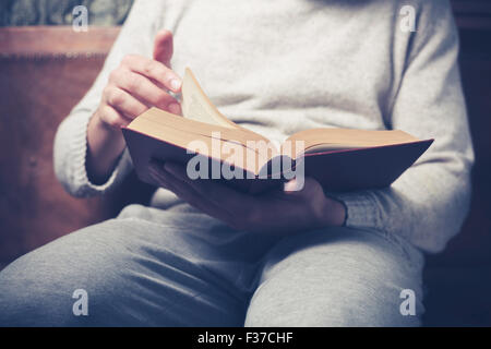 Young man is sitting on a sofa and flipping the pages of a big book Stock Photo