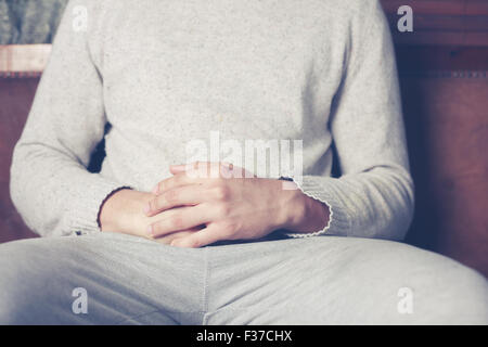 Young man with his hands resting on his belly is relaxing on sofa Stock Photo