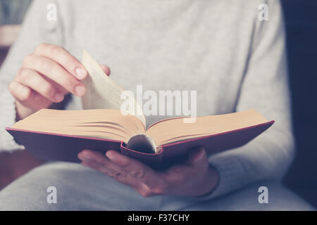 Young man is sitting on a sofa and flipping the pages of a big book Stock Photo