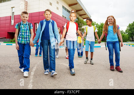 Happy children carry rucksacks, walk near school Stock Photo