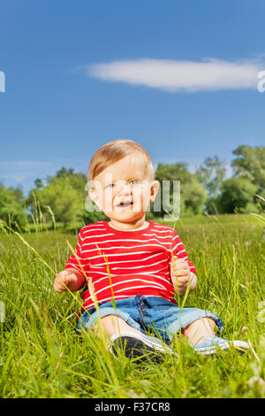 Smiling baby sitting on the green grass alone Stock Photo