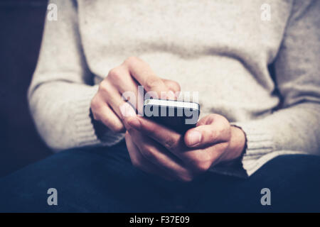 Closeup on a man's hands as he is sitting on a sofa and using a smartphone Stock Photo