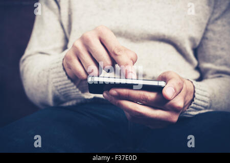 Closeup on a man's hands as he is sitting on a sofa and using a smartphone Stock Photo