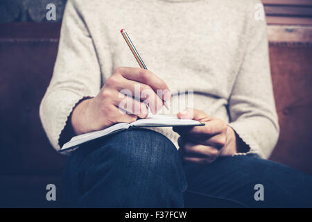 A man is sitting on a sofa and writing notes in a notebook Stock Photo