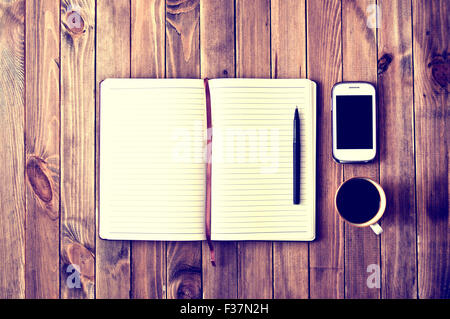 White cell phone, pen, cup of coffee and notebook on wooden table. Work space. Instagram vintage picture. Stock Photo