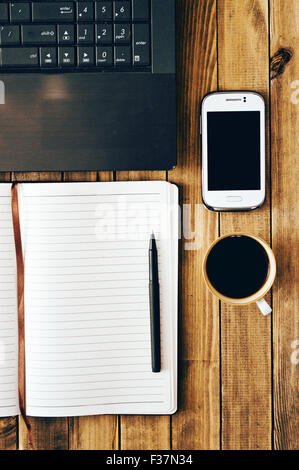 White cell phone, pen, cup of coffee computer and notebook on wooden table. Work space. Instagram vintage picture. Stock Photo
