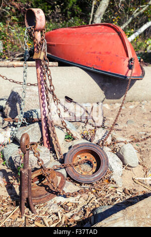 Old red rowboat lays on the coast near rusted anchors and chains Stock Photo