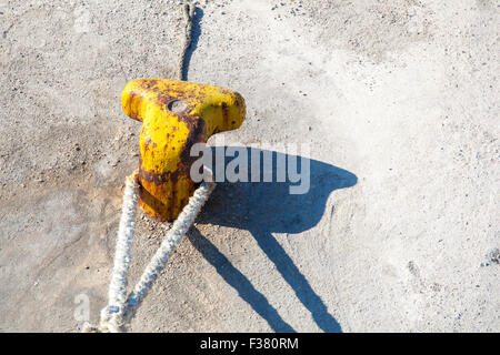 Strong metal mooring bollard with a ship safety rope on a concrete pier. Stock Photo