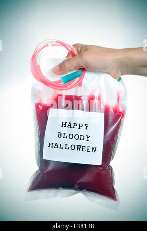 closeup of the hand of a young man holding a blood bag with a label with the text happy bloody halloween written in it, with a s Stock Photo
