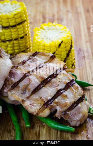 Grilled piece of pork with green beans and corn cobs, on wooden chopping board. Stock Photo
