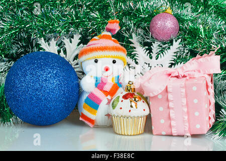 Snowman with blue ball, pink gift box and white snowflake on a background of green garland Stock Photo