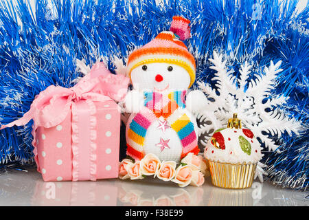 Snowman with pink gift box and white snowflakes on a background of blue garland Stock Photo