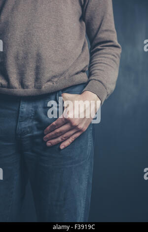 A young man is standing against a black background with his hand in his pocket Stock Photo