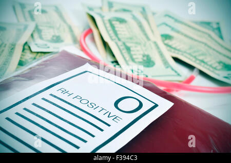 closeup of a blood bag with a label with the text O RH positive and a pile of US dollar bills in the background Stock Photo