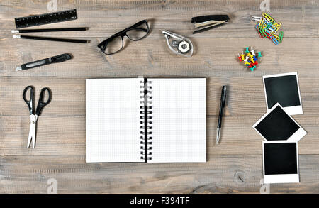 Office and school supplies over wooden desk background. Open book, polaroid photo frames and writing tools. Vintage style toned Stock Photo