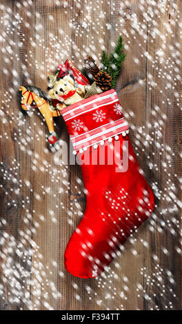 Christmas stocking with old toys decoration and pine branch over wooden background. Nostalgic vintage style picture with falling Stock Photo