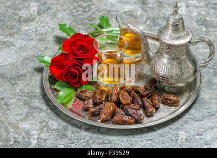 Tea, dates fruits and red rose flowers. Islamic holidays decoration. Eid al-Fitr. Oriental hospitality concept. Slective focus Stock Photo