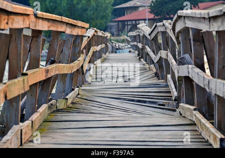 Closeup of a deformed and dilapidated wooden bridge over the river Stock Photo