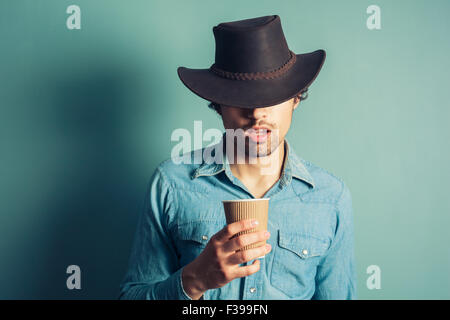 Young cowboy is drinking coffee from a paper cup Stock Photo