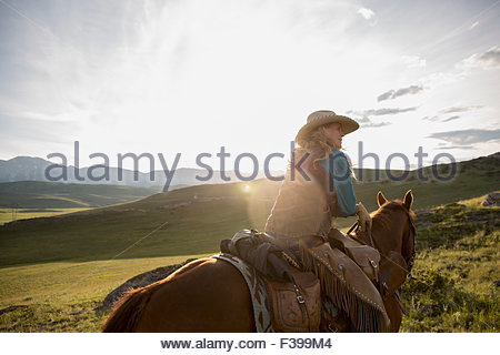 Female rancher horseback riding in remote sunny field