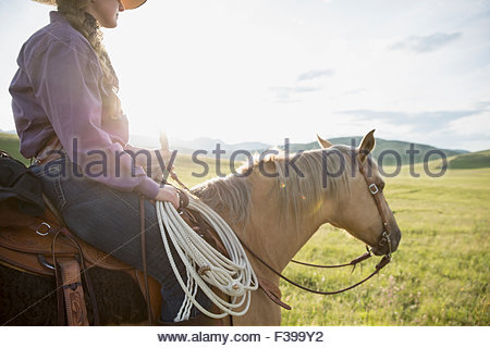 Female rancher horseback riding in sunny remote field