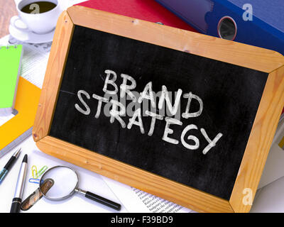 Brand Strategy - Chalkboard with Hand Drawn Text, Stack of Office Folders, Stationery, Reports on Blurred Background. Toned Imag Stock Photo