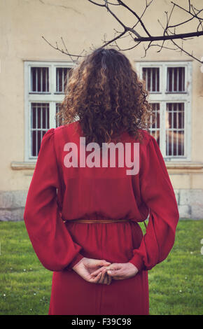 Woman in red dress standing outdoors, rear view Stock Photo