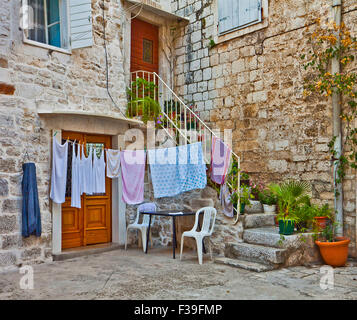 staircase full of plants and flowers leads to a Dalmatian house made of white stone blocks with laundry hanging behind Stock Photo