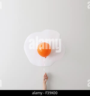 Woman holding a balloon against a wall creating a Conceptual fried egg Stock Photo