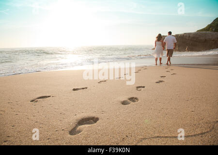 Rear view of a Young couple walking barefoot on the beach at sunset, Laguna Beach, Orange County, California, USA Stock Photo