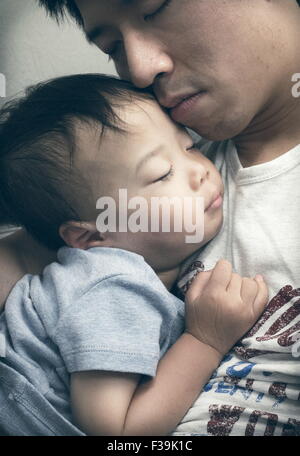 Portrait of a man with his eyes closed holding his sleeping son Stock Photo
