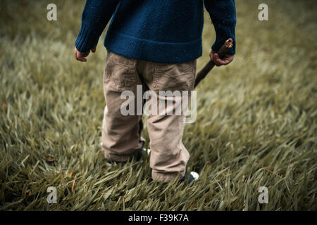 Low section of a toddler standing in field holding a wooden stick Stock Photo