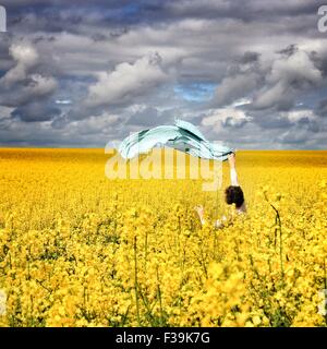 Woman standing in a rapeseed field waving a scarf in the air Stock Photo
