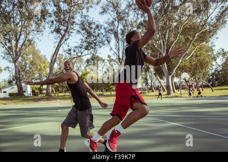 Two young men playing basketball, shooting hoops in the park at sunset Stock Photo