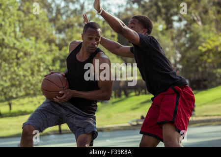 Two young men playing basketball in the park at sunset Stock Photo