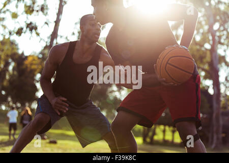 Two young men playing basketball in the park at sunset Stock Photo
